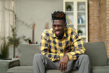 Sick man at home. Young African man sitting on sofa feeling unwell.