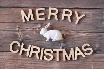 Merry Christmas inscription from wooden letters. Hare as a symbol of 2023. Wooden table, film grain.