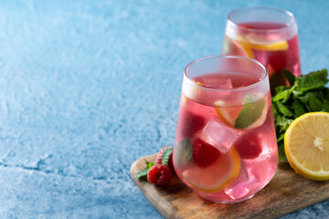 Raspberry lemonade drink in glass on blue background. Copy space
