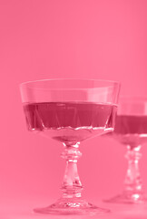 Two crystal glasses of sparkling wine or champagne. Toned image in trendy magenta color of year 2023. Minimal creative composition with copy space.