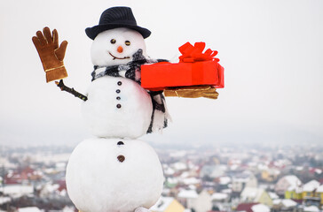 Happy snowman with present gift box waving hand. Merry christmas and happy new year greeting card.