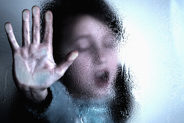 Portrait of scared young girl making NO sign, showing hand STOP gesture. Kid standing behind wet glass and says No to domestic violence, abuse, school bullying,  problem concept. Copy space.