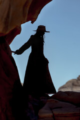 Silhouette of a girl wearing a long dress and a hat on a rocky landscape  in Alula, Saudi Arabia 