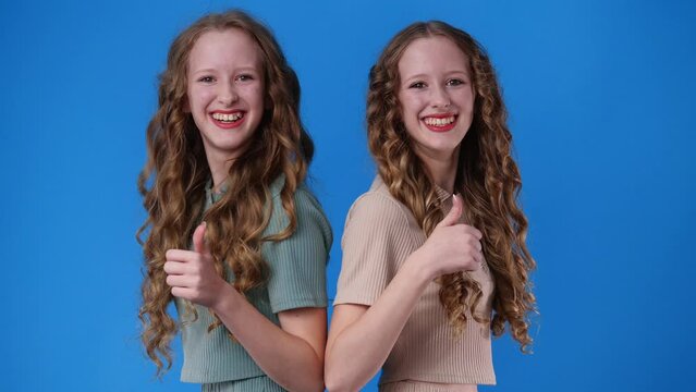 4k video of two twin girls showing thumbs up over blue.