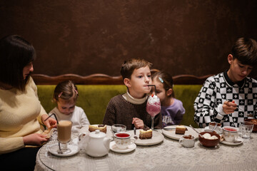 Happy family eating desserts together at cozy cafe and having fun. Boy kid drink milk shake.
