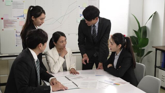 asian female manager sharing ideas with hand gestures in corporate group meeting at workplace. members nodding head showing approval while listening