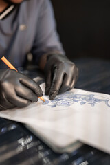 A tattoo artist is drawing a design stencil on his work stretcher before tattooing