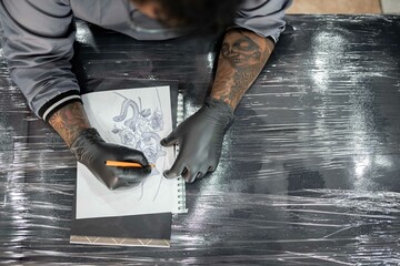 A tattoo artist is drawing a design stencil on his work stretcher before tattooing