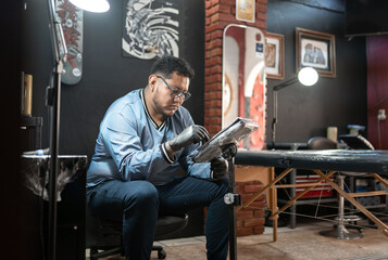 A tattoo artist is checking out his designs on his work tablet in his studio