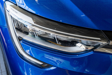 Fototapeta premium Blue SUV Renault Arkana. Right view. Showroom in Renault dealership. Close-up right front headlight. Foreground. Mega Adygea. Krasnodar, Russia - August 04, 2022