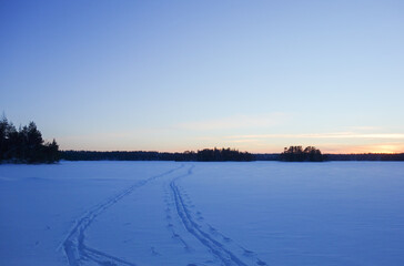 Winter landscape on snowy lake ice with ski tracks in the snow in the blue hour
