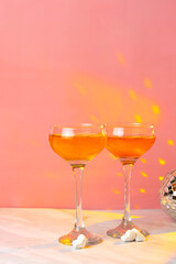 Orange cocktail with tall glasses on a pink background. Two glasses