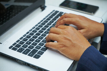 picture of an Asian business man hands working in office with laptop computer, typing on keyboard at his desk, close up           