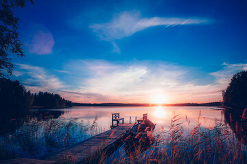 Sunset on a lake. Wooden pier with fishing boat at sunset in Finland