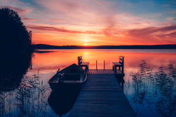 Zonsondergang op een meer. Houten pier met vissersboot bij zonsondergang in Finland