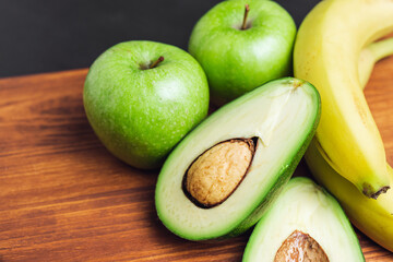 Sliced halves of avocado, banana and apple fruits on a wooden board, ingredients for cooking