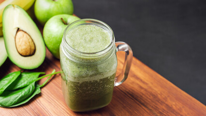 Green smoothie drink blended in a glass jar, avocado, spinach leaves and apples at wooden board