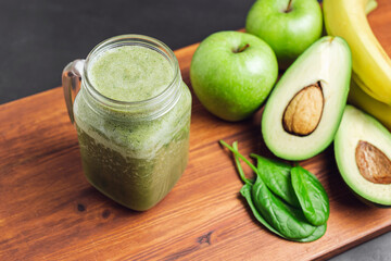 Green smoothie drink blended in a glass jar, avocado, spinach leaves, banana and apples at wooden...