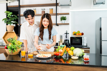 A happy couple prepares and cooks healthy salad with vegetables on a cutting board together in the home kitchen. Food cooking for young couple husband and wife in a good mood and healthy relationship.