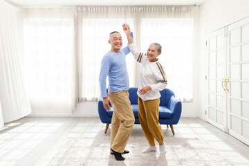 Romantic and cheerful Asian well-being senior couple enjoy dancing and holding hands to music together with smiles and happiness in the living room. Senior retirement activity at home. - Powered by Adobe