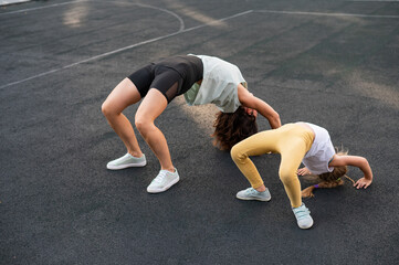 A little girl and her mom do a bridge exercise at the outdoor sports ground. 