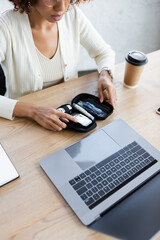 Fototapeta premium Cropped view of african american businesswoman holding diabetes kit near laptop and coffee in office
