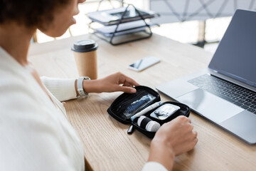 Cropped view of african american businesswoman holding diabetes kit near gadgets and coffee in...