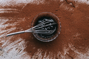 Fototapeta premium Melted chocolate and whisker on bowl against scattered cocoa powder