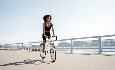 A curly-haired happy woman rides a bicycle. A millennial cyclist rides on environmentally friendly...