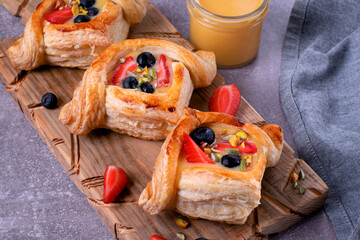 Puff pastry buns with custard, strawberry and blueberry served on wooden board - 556684293