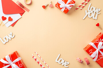 Valentine's Day concept. Top view photo of red gift boxes envelope with letter inscriptions love straws decorative tape and clips on isolated pastel beige background with copyspace in the middle