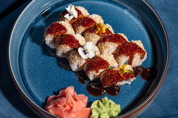 Sushi on blue velvet couch background. Maki roll with salmon, flower petals and teriyaki sauce on blue plate. Modern, stylish Japanese cuisine. Oriental restaurant menu. Close up, space for design