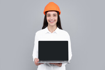 Positive smiling woman in protective helmet with laptop computer isolated on grey background. Architect woman wear helmet and shirt. Business woman, construction manager, builder.