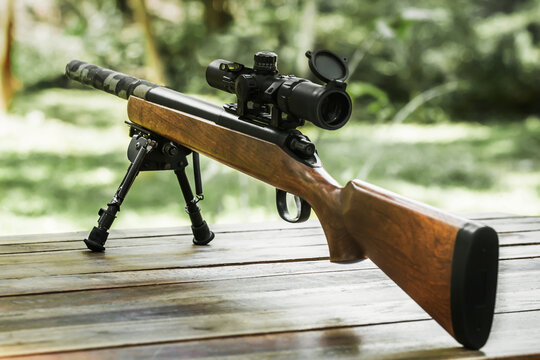Wooden bolt action short sniper rifle with scope and bipod standing on wooden table