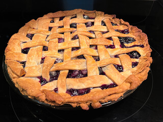 Homemade blueberry pie with golden flakey lattice crust and black background.