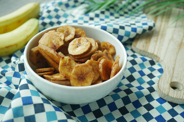  dry banana chips in a bowl on black tiles background 