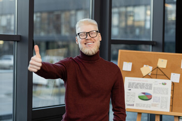 bearded albino businessman in glasses smiling and showing thumb up in office