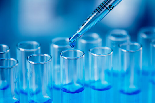 Test tubes with blue liquid water samples and pipette over blue background. Pipette dropping sample into test tube. Laboratory glassware, science laboratory research concept.