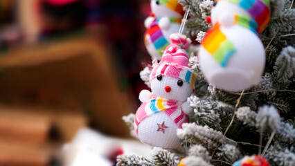Tiny figurine snowman in colorful outfit in front of snowy pine tree, blurred background, with space and text space