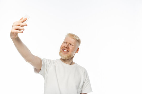 cheerful albino man in t-shirt taking selfie on smartphone on white background