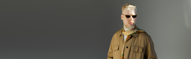 sunlight on face of stylish albino man in sunglasses and shirt jacket on grey, banner