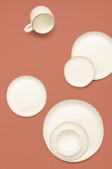 Creative arrangement of plates, bowl and a cup on pastel pink background. Minimal white ceramic dinnerware.