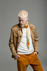 albino man in stylish shirt jacket and silk scarf standing with hands in pockets isolated on grey