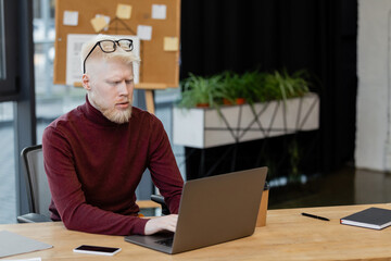 bearded albino businessman using laptop near smartphone with blank screen in office