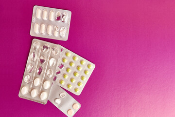 Pills of different shapes and colors on a pink background.
