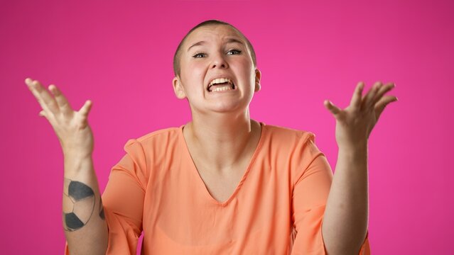 Angry, scared young gender fluid non binary woman 20s put hands on head screaming crying ask why me, isolated on pink background studio.