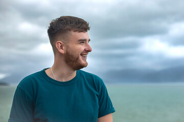 Profile side photo of handsome happy guy, young man enjoying sea, ocean view, landscape, looking into distance at summer day in tropical country at storm with cloudy sky, breathing deep fresh air