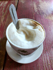 Tasty and creamy cappuccino coffee in a beautiful cup on a raw wood amaranth table. Italian breakfast concept. Close up view.
