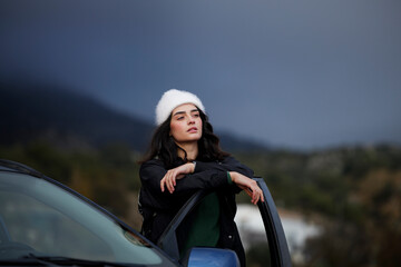 Young woman leaning on the car door. Happy traveler in the car enjoying the view
