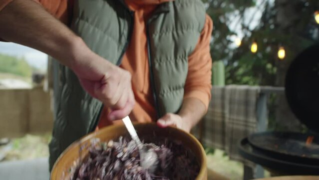 Culinary blogger mixing red cabbage cole slaw salad in bowl and talking while cooking food on outdoor terrace